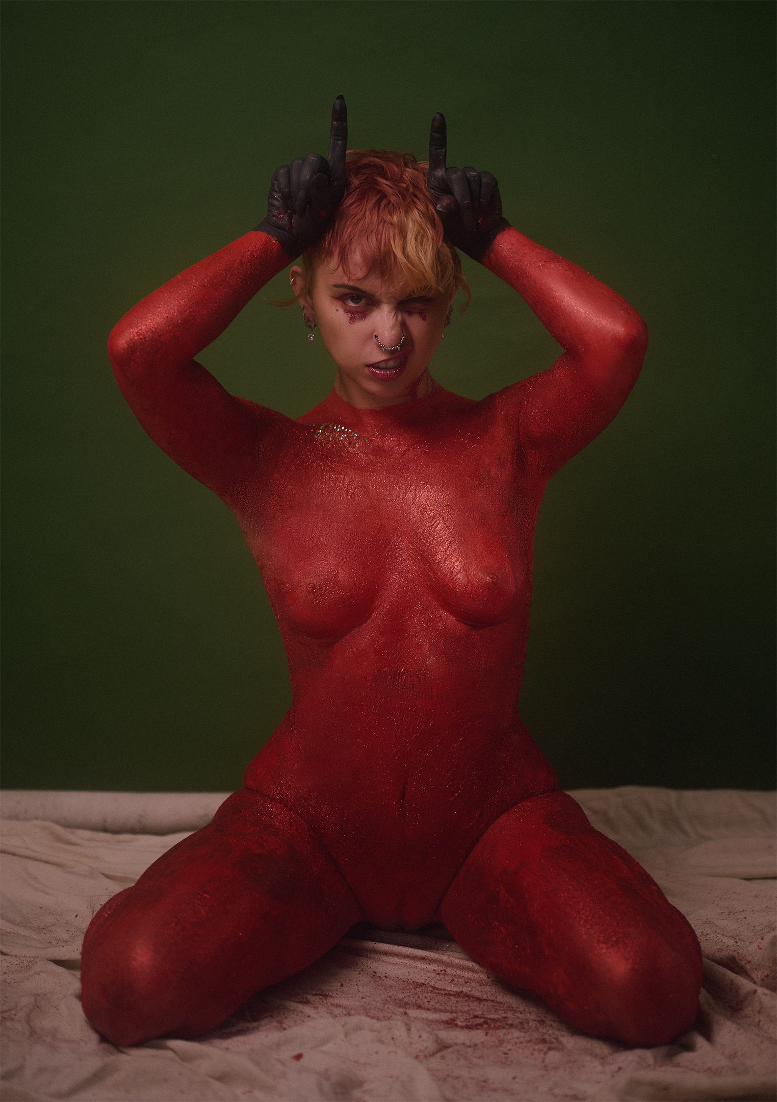 A woman kneeling covered in red body paint and glitter.